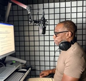 William Marshall Cline Voice acotr and narrator, seated in his home studio wearing headphones in front of microphone