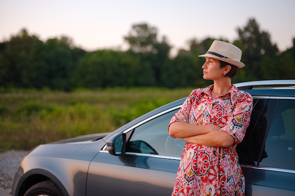 A woman with a hat, leaning on her new car looking out across the landscape